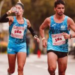 Two athletes participating in a marathon, hydrating and focused, while running outdoors on a city street.